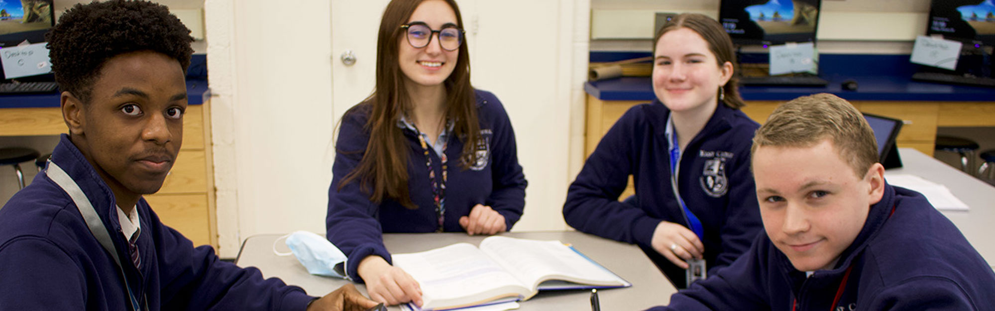Four happy students sitting at a table together - East Catholic Fall Open House - Thursday, October 6 at 6:30 p.m.