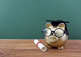 Gold piggy bank wearing a mortarboard with a diploma beside it