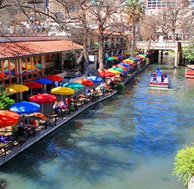 colorful tables and umbrellas next to river with boat